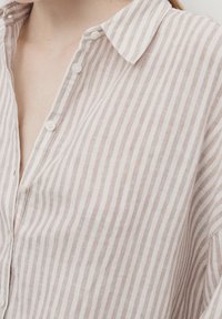 Gros plan d'une personne portant une chemise boutonnée à rayures verticales beige et blanche avec un col ouvert.