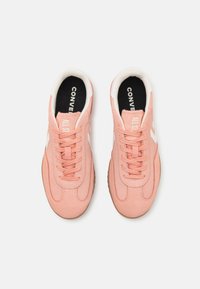 Baskets en suède rose clair avec des accents blancs, fermeture à lacets et semelles en caoutchouc. Présente le marquage "CONVERSE ALL STAR" sur les semelles intérieures.