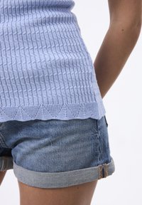 Top azzurro chiaro in maglia a coste con un design a scollatura ondulata, abbinato a pantaloncini in denim arrotolati con risvolto azzurro chiaro.