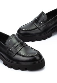 Czarne skórzane mokasyny z masywnymi gumowymi podeszwami, z obcisłymi srebrnymi ćwiekami wzdłuż górnych krawędzi i detalem na pasku.