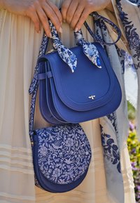 Plava kožna torba s strukturiranim oblikom, koja ima odvojivu torbicu za preko ramena s cvjetnim uzorkom i naglaske s maramom.