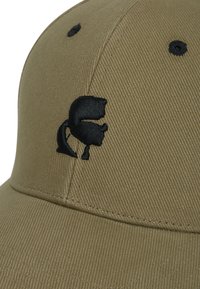 Gorra verde oliva hecha de tela texturizada, con un destacado logo negro bordado en la parte frontal y seis ojales de ventilación.