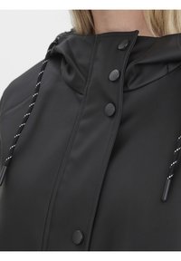 Giacca nera impermeabile con colletto alto, bottoni a scatto e cappuccio con cordino, caratterizzato da un cordino bianco e nero in contrasto.