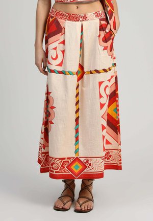 Pantalon à jambes larges taille haute avec des motifs géométriques et floraux audacieux en rouge, orange et sarcelle, porté avec des sandales plates marron à lanières.