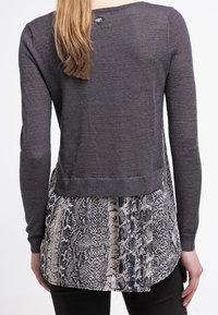 Gray knit sweater with long sleeves, featuring a textured snake print bottom panel in black and white. Rounded hemline at back.