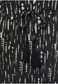 Tissu à motifs noir et blanc avec des rayures verticales abstraites, une taille froncée et des accents de liens avec pompons noirs.