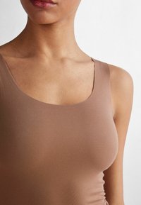 Brązowy dopasowany top na ramiączkach z okrągłym dekoltem, gładką teksturą i szerokimi ramiączkami, podkreślający bezszwowy design i dopasowany krój.