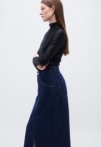 Μαύρο πουλόβερ με υφή και ψηλό γιακά, σε συνδυασμό με μακριά σκοτεινή τζιν φούστα με πλαϊνές τσέπες και εμπρόσθια σχισμή.