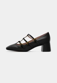 Black leather high-heeled shoe featuring a pointed toe, three decorative straps, gold buckles, and a square block heel.