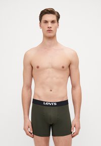 Maslinaste zelene bokserice s crnim elastičnim pojasom na kojem se nalazi bijeli "Levi's" logotip. Dizajn je uštogljen i izrađen od glatkog materijala.