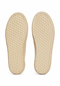 Chaussures slip-on beiges avec une tige en toile texturée et des semelles en caoutchouc dotées d'un motif tissé pour une meilleure adhérence. Design classique sans marquage visible.