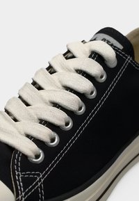 Μαύρο πανί αθλητικό παπούτσι με λευκά παχιά κορδόνια, μεταλλικά ρούχα, λευκή ραφή και λευκή λαστιχένια σόλα.