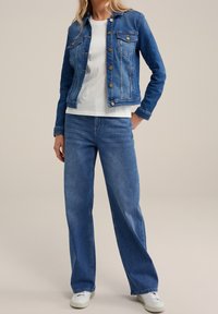 Jeansjacka med knappframsida, två bröstfickor och en något figursydd form. Matchad med ljusblå vida jeans och vita sneakers.