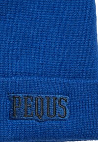 Gorro de punto azul con una tela texturizada. Presenta un logotipo bordado en negro "PEQUUS" en un parche cosido.