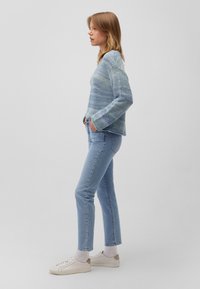 Gestreifter Strickpullover in Blau und Grün, lockere Passform, lange Ärmel, kombiniert mit hellblauen geraden Jeans und weißen Sneakers, Seitenansicht.