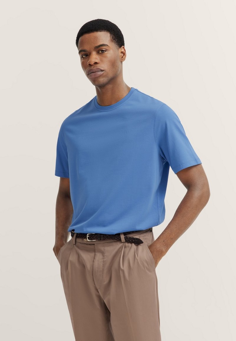 Blue short-sleeve shirt made of a smooth, lightweight fabric, paired with light brown trousers and a braided black belt.