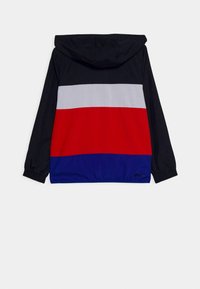 Giacca con cappuccio nera, con strisce orizzontali in rosso, grigio e blu. Tessuto leggero con polsini e orlo elastici.