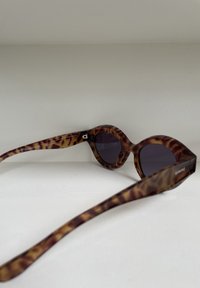 Occhiali da sole tartarugati con lenti scure, forma arrotondata oversize e tempie parallele con un logo del marchio inciso sul lato.