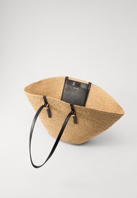 Geweven rieten tote bag met een zwart binnenzak. Voorzien van zwarte leren hengsels en een gestructureerd oppervlak, gevormd als een brede kegel.