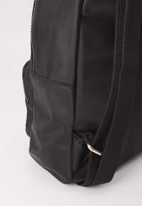 Zaino in nylon nero con superficie testurizzata, dotato di una tasca laterale, tracolla regolabile e dettagli in hardware dorato.