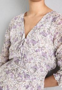 Floral-patterned dress in light fabric. Features a V-neckline, drawstring detail, and puff sleeves. Colors include lavender, cream, and beige.