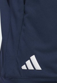 Mørkeblått stoff med en glatt tekstur har en hvit Adidas-logo med tre diagonale striper nær nederste høyre hjørne.