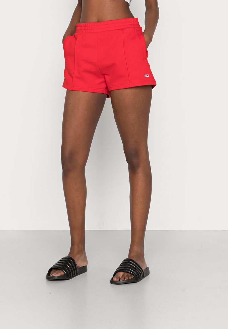 Shorts de sport rouges avec une taille élastique, deux poches latérales et un petit logo en accent. Assortis à des sandales noires à brides.
