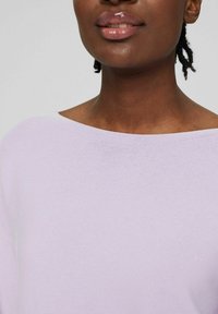 Ein lilafarbener, gestrickter Pullover mit einem weiten Ausschnitt, strukturiertem Stoff und einer lockeren Passform, getragen über einem glatten, dunklen Hautton.
