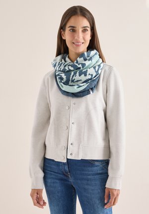 Sweat-shirt gris clair avec une fermeture à boutons sur le devant, accompagné d'une grande écharpe à motifs bleus et verts enroulée autour du cou. Jean en denim visible.