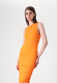 Robe sans manches orange avec texture froncée, design ajusté et décolleté asymétrique, fabriquée à partir d'un tissu lisse et extensible.