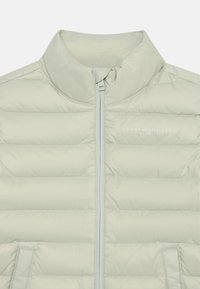 Casaco puffer verde claro com gola alta, fecho de correr na frente, padrão de acolchoado horizontal e pequeno bolso lateral. Logótipo impresso no peito.