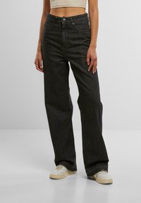 Hoch taillierte, weit geschnittene schwarze Jeans aus Denim mit glatter Textur, fünf Taschen und dezenten Nähten. Mit einem vorderen Knopfverschluss.