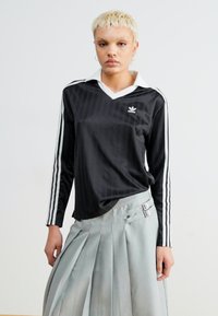 Μαύρο πουκάμισο με μακριά μανίκια και λευκό γιακά, με κατακόρυφες ρίγες και τρεις λευκές πλευρικές ρίγες. Εμβληματικό λογότυπο στο στήθος.