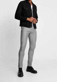 Svart denimjacka, grå mönstrade slim-fit byxor, svarta snörskor och en vit t-shirt som visar upp en modern avslappnad stil.