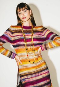 Mehrfarbiges gestreiftes Strickkleid mit lebendigen Farbtönen in Orange, Lila und Gelb, mit langen Ärmeln und einem hohen Kragen. Aussagekräftige Perlenkette.