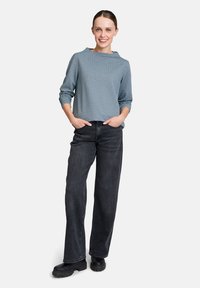 Blau gemusterte Langarmbluse mit weitem Halsausschnitt, kombiniert mit lockeren schwarzen Denim-Hosen und klobigen schwarzen Stiefeln.