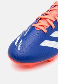 Modrá fotbalová kopačka s texturovaným syntetickým svrškem, oranžovými tkaničkami a bílými pruhovanými akcenty. Má zaoblenou špičku a tvarované kolíky.