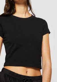 Svart kortärmad t-shirt i mjuk bomull med rund halsringning och korta ärmar. Plagget sitter tajt och slutar ovanför midjan.