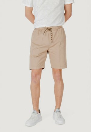 Pantaloni corti beige con vita elastica e coulisse, caratterizzati da una superficie liscia e un taglio al ginocchio. Abbinati a sneakers bianche.