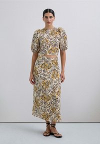 Conjunto de dos piezas que incluye un top corto con mangas abullonadas y una falda de talle alto. La tela tiene un estampado de animal en amarillo y marrón.