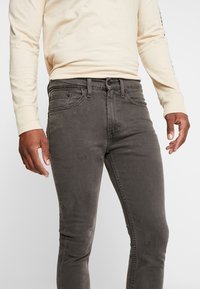 Jeans de mezclilla gris con un diseño ajustado, que cuentan con un estilo clásico de cinco bolsillos y remaches de metal, combinados con una camiseta de manga larga ligera.