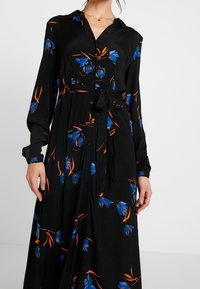 Robe noire à manches longues avec des motifs floraux bleus et oranges, un devant à boutons et une ceinture à nouer à la taille. Texture de tissu lisse.