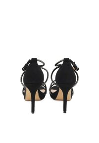 Sandali con tacco alto in suede nero, caratterizzati da un design a strisce con accenti metallici, punta affusolata e tacchi a stiletto sottili.