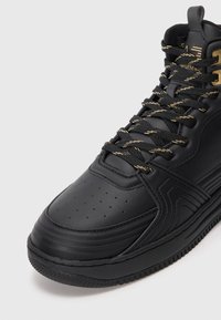 Fekete magas szárú bőr sneakers, sima felülettel, perforált orral és arany díszítésű fűzőkkel, valamint textúrázott részletekkel az oldalán.