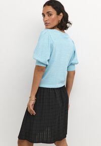 Light blue short-sleeve knit sweater with textured fabric; paired with a mid-length black skirt featuring subtle vertical stripes.