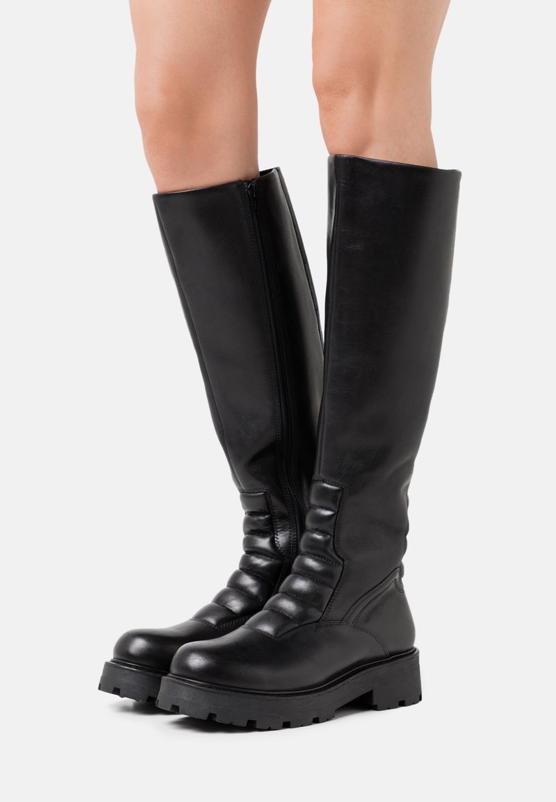 Botas de piel negra hasta la rodilla con suela gruesa, con cremallera lateral, detalles fruncidos a lo largo del eje y textura suave.