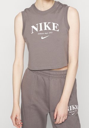Osoba nosząca dopasowany szary bezrękawnik typu crop top oraz spodnie dresowe z białymi logo Nike i tekstem "Athletic dept. 1972" na obu elementach odzieży.