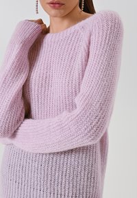 Maglione rosa chiaro lavorato a maglia con maniche lunghe, caratterizzato da una texture a coste e una vestibilità ampia. Messo in risalto da un ampio scollo a girocollo.