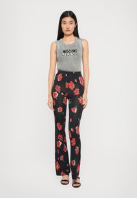 Grå ribbet tanktopp med teksten "Moschino Jeans", kombinert med svarte vide bukser med rødt blomstermønster. Enkle svarte sandaler.