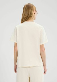 Camiseta de manga corta en crema, de suave algodón y corte relajado, con escote redondo y detalles de costura simples.